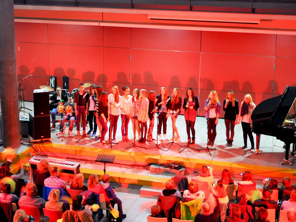 Chor singt in rotem Licht vor dem Flügel.